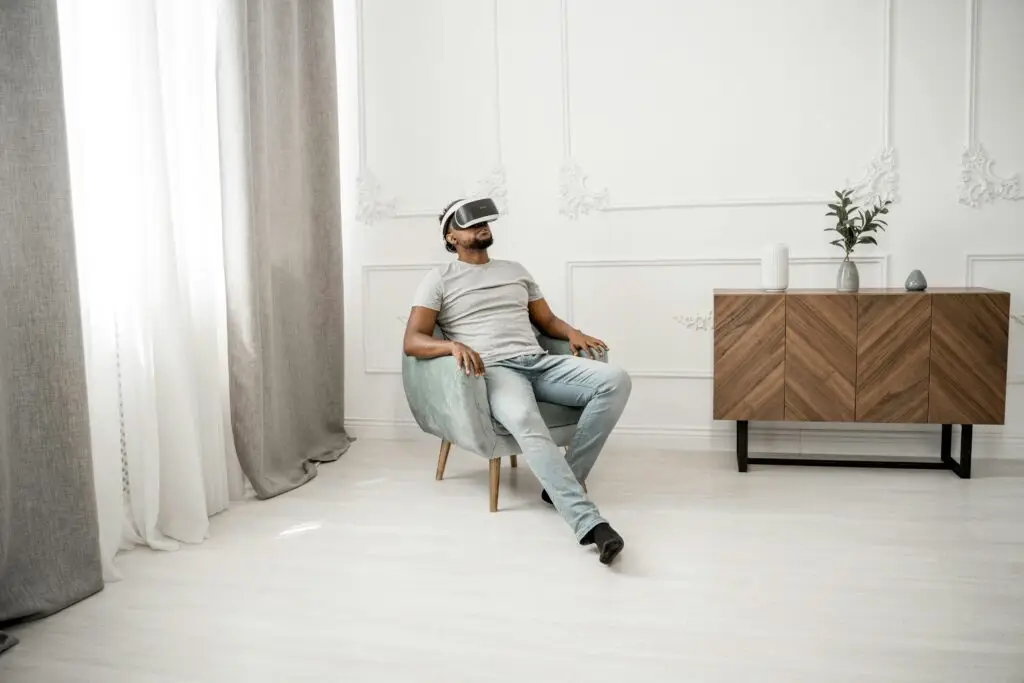 A man sits comfortably on a chair indoors, experiencing virtual reality with VR glasses.